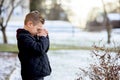 Cute little boy praying with closed eyes in the middle of the winter park