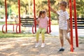Cute little boy pushing his sister on swings outdoors
