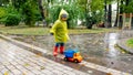 Cute little boy in raincoat and rubber boots blaying with toy truck in big puddle at park Royalty Free Stock Photo