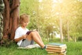 Cute little boy reading book on green grass near tree in park Royalty Free Stock Photo