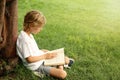 Cute little boy reading book on green grass near tree in park Royalty Free Stock Photo