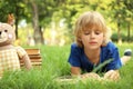 Cute little boy reading book on green grass in park Royalty Free Stock Photo