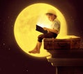 Cute little boy reading a book in the moon light