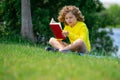 Cute little boy reading book in park. Kid sit on grass and reading book. Kid boy reading interest book in the garden Royalty Free Stock Photo