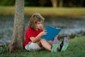 Cute little boy reading book in park. Kid sit on grass and reading book. Kid boy reading interest book in the garden Royalty Free Stock Photo