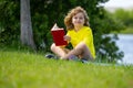 Cute little boy reading book in park. Kid sit on grass and reading book. Kid boy reading interest book in the garden Royalty Free Stock Photo