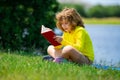 Cute little boy reading book in park. Kid sit on grass and reading book. Kid boy reading interest book in the garden Royalty Free Stock Photo