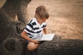 Cute little boy reading book on tree in park Royalty Free Stock Photo