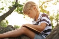 Cute little boy reading book on tree in park Royalty Free Stock Photo