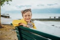 Cute little boy resting on a bench by the lake on a very windy day