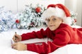 cute little boy in Santa Claus hat writes letter to Santa Claus to get gift lying on bed against background of Christmas Royalty Free Stock Photo