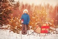 Cute little boy in Santa hat carries a wooden sled with gifts in snowy forest