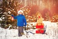Cute little boy in Santa hat carries a wooden sled with gifts in snowy forest