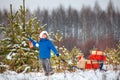 Cute little boy in Santa hat carries a wooden sled with gifts in snowy forest