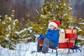 Cute little boy in Santa hat carries a wooden sled with gifts in snowy forest