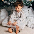 Cute little boy sitting with a box of gifts around the Christmas tree. Adorable blonde caucasian toddler. Square photo