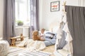 Cute little boy sitting in comfortable bed playing with teddy bear, real photo of natural playroom interior Royalty Free Stock Photo