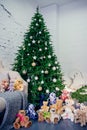 Cute little boy sitting down by the decorated Christmas tree with toys, teddy bears and gift boxes Royalty Free Stock Photo