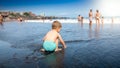 Cute little boy sitting on the ocean beach and waiting for the sea wave Royalty Free Stock Photo