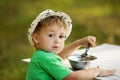 Cute little boy sitting at table and eating in countryside
