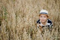 Cute little boy in a straw hat is sitting on an oat field playing hide and seek. Funny kid hiding in a field with oats. Royalty Free Stock Photo