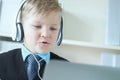 Cute 6 year old boy in suit listening to music or audio tutorial on headphones at the office background. Royalty Free Stock Photo