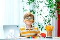 Cute little boy thinking about something. Funny pupil with pencil in mouth doing homework with tablet laptop computer Royalty Free Stock Photo