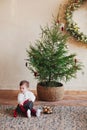 Little boy sitting on carpet under small decorated christmas tree while unwrapping gift Royalty Free Stock Photo