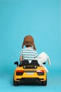 Cute little boy with toy bunny driving children`s car on light blue background, back view Royalty Free Stock Photo