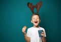 Cute little boy with toy reindeer horns holding cup of hot chocolate and cookie on color background Royalty Free Stock Photo