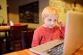 Cute little boy watching cartoon movie using computer in the cafe or restaurant. Child communication by social net or messenger