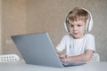 Cute little boy is watching cartoons or a movie on a laptop. Caucasian child sits at a table at home and listens to Royalty Free Stock Photo