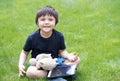 Cute little boy watching his tablet and playing with teddy bear in the garden in a sunny day, Portrait of Happy kid sitting on gre Royalty Free Stock Photo