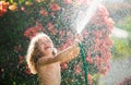 Cute little boy watering flowers in the garden at summer day. Child farmer with garden hose in planting plant. hose Royalty Free Stock Photo