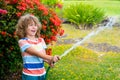 Cute little boy watering flowers in the garden at summer day. Child using garden hose. Funny kid watering plants in the Royalty Free Stock Photo