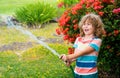 Cute little boy watering flowers in the garden at summer day. Child using garden hose. Funny kid watering plants in the Royalty Free Stock Photo