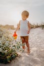 Cute little boy watering plants with can on sandy beach. summer sunny day. Toddler with colorful pot. Natural aestetic Royalty Free Stock Photo