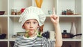 Cute little boy wearing chef hat pointing up with hand. Chef has great idea at the kitchen. Child want to be a professional chef