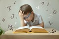 Cute little boy wearing glasses, open book in front of him, letters around, learn foreign language, dyslexia concept Royalty Free Stock Photo