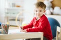 Cute boy wearing red sweater sitting at small wooden table Royalty Free Stock Photo