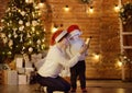 Cute little boy wearing Santa hat and his mother or grandmother regard a Christmas gift. Portrait of happy family on Christmas eve