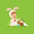 Cute little boy in a white bunny costume sitting and playing with basket with painted eggs, kid having fun on Easter egg Royalty Free Stock Photo