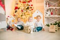 Cute little boys with blond hair plays with little girl in a bright room decorated with Christmas garlands