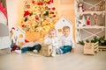 Cute little boys with blond hair plays with little girl in a bright room decorated with Christmas garlands