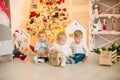 Cute little boys with blond hair plays with little girl in a bright room decorated with Christmas garlands