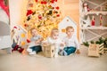 Cute little boys with blond hair plays with little girl in a bright room decorated with Christmas garlands