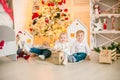 Cute little boys with blond hair plays with little girl in a bright room decorated with Christmas garlands