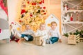 Cute little boys with blond hair plays with little girl in a bright room decorated with Christmas garlands