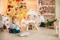 Cute little boys with blond hair plays with little girl in a bright room decorated with Christmas garlands