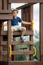 A cute little brave boy sitting at the top of the wooden playground
